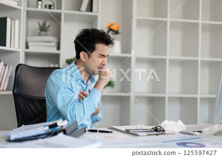 Office Worker Struggling with Cold Symptoms at Desk in Modern Workplace Environment Office Worker Struggling with Cold Symptoms at Desk in Modern Workplace Environment 125597427