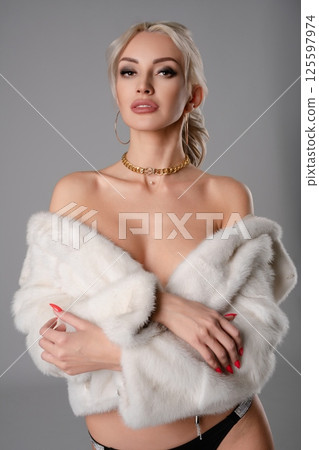 Elegant woman in stylish lingerie and a fur coat poses confidently indoors 125597974