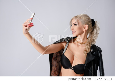 Confident woman poses for selfie in stylish lingerie and jacket 125597984
