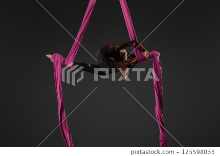 Girl performs aerial gymnastics using pink fabric suspended from a pole Girl performs aerial gymnastics using pink fabric suspended from a pole 125598033