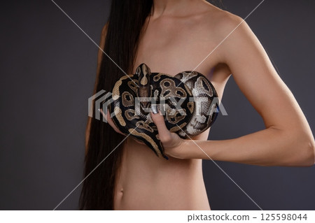 Woman posing topless with a snake in an artistic, intimate setting Woman posing topless with a snake in an artistic, intimate setting 125598044