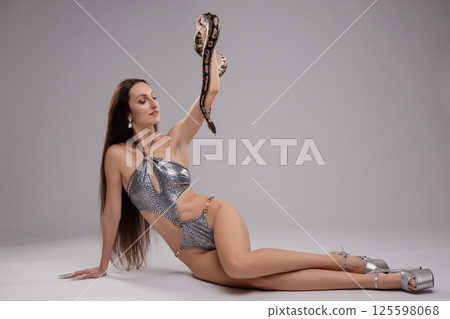 Elegant woman poses with a snake while showcasing intricate lingerie design 125598068