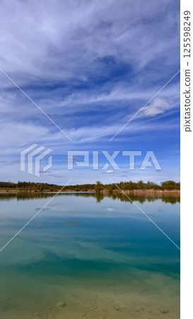 Tranquil lake reflecting blue sky with clouds and lush greenery surrounding the serene water concept Tranquil lake reflecting blue sky with clouds and lush greenery surrounding the serene water concept 125598249