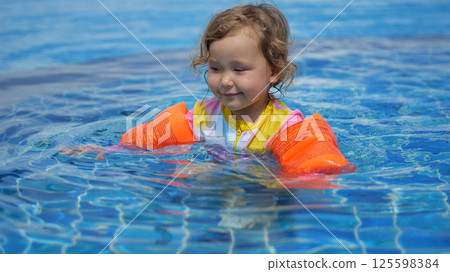Little girl learning to swim with armbands in a pool 125598384