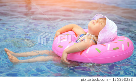 Girl in brightly colored inflatable ring enjoys warm water of pool 125598388