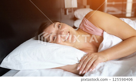 Woman sleeping peacefully and waking up smiling in hotel room 125598406