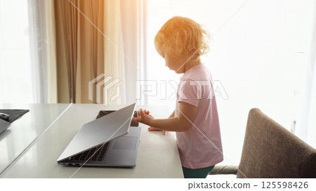 Curious toddler girl exploring laptop at hotel room table 125598426