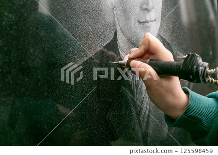 The hand of a female artist who applies images to monuments by hand engraving. 125598459
