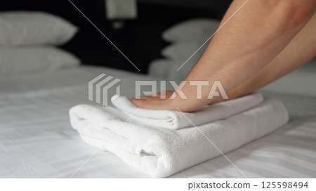 Woman housemaid puts clean towels onto bed with bedclothes 125598494
