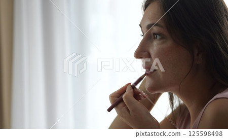 Woman applying lip pencil in hotel room 125598498