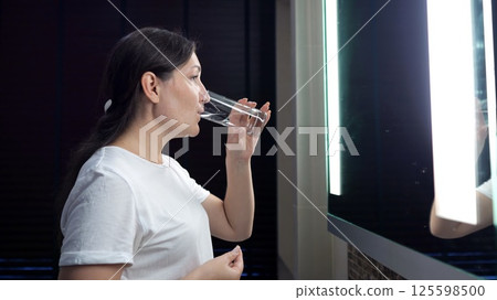 Woman drinking water in bathroom mirror reflection 125598500