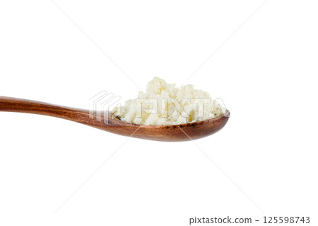 Close-up of crumbly cottage cheese on a wooden spoon on a white background. 125598743