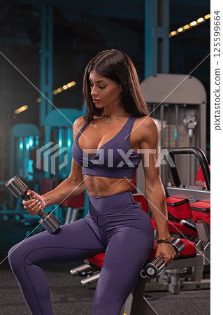 In well equipped gym fitness enthusiast focuses on weight training dumbbells. space has modern equipment and lighting creates energetic atmosphere. In well equipped gym fitness enthusiast focuses on weight training dumbbells. space has modern equipment and lighting creates energetic atmosphere. 125599664