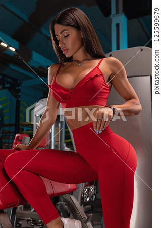 dedicated individual wearing vibrant red workout outfit poses confidently gym showcasing determination and commitment fitness in modern environment. dedicated individual wearing vibrant red workout outfit poses confidently gym showcasing determination and commitment fitness in modern environment. 125599679