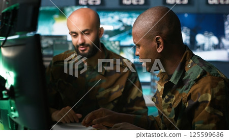 Air force officer and coworker talking while performing tactical level surveillance in command post. Teamworking military professionals using radar equipment to look at assault zones, camera A Air force officer and coworker talking while performing tactical level surveillance in command post. Teamworking military professionals using radar equipment to look at assault zones, camera A 125599686