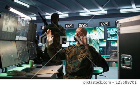 Military agent using augmented reality tech in control room, analyzing aerial reconnaissance data. Intelligence corps expert controlling drones attacking strategic targets using AR hologram, camera B Military agent using augmented reality tech in control room, analyzing aerial reconnaissance data. Intelligence corps expert controlling drones attacking strategic targets using AR hologram, camera B 125599701