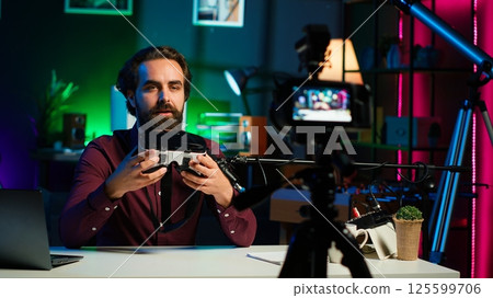 Close up shot of futuristic VR goggles held by man reviewing them for viewers. Internet star filming technology channel vlog for gadget enthusiasts, showcasing virtual reality headset, camera A 125599706