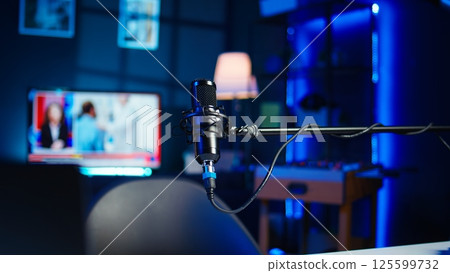 Close up of podcast microphone used to record videos for online show. Zoom in shot of streaming sound capturing and recording podcasting mic in empty living room with neon lights 125599732