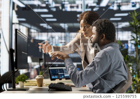 Young employee and manager gathered around a computer discussing objectives and strategizing solutions to solve administrative tasks faster. Aligning business goals and milestones. Young employee and manager gathered around a computer discussing objectives and strategizing solutions to solve administrative tasks faster. Aligning business goals and milestones. 125599755