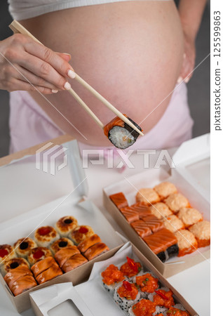 A pregnant woman stands at a table with rolls. Close-up of the belly. 125599863
