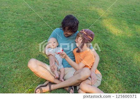 Father with his two sons in the park, the older boy wearing a pilot hat and holding a toy airplane while the baby watches. Childhood, bonding, and family adventure concept 125600371