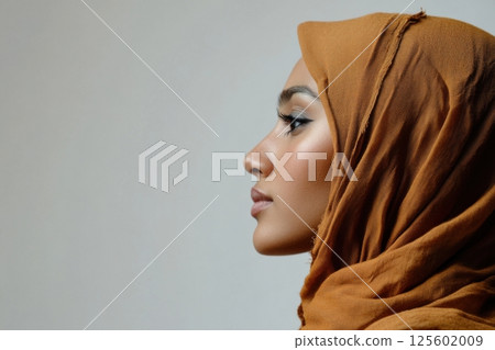 Beautiful profile of a woman wearing a brown hijab against a neutral background in a soft light setting 125602009