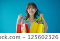 Happy young woman smiles holding colorful shopping bags against blue background. 125602326