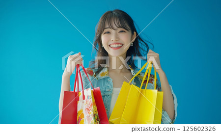 Happy young woman smiles holding colorful shopping bags against blue background. Happy young woman smiles holding colorful shopping bags against blue background. 125602326