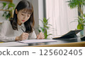 A young woman attentively writes notes at her desk in a bright office. 125602405