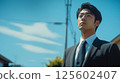 Young businessman in suit looks up thoughtfully on sunny day outdoors. 125602407