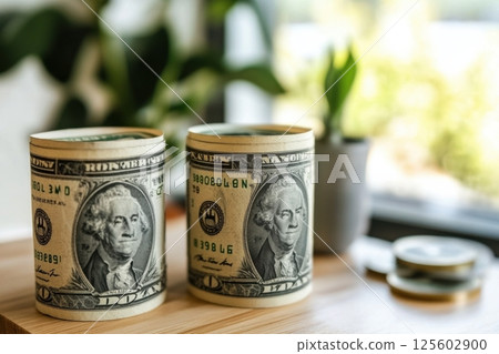 Currency rolls and coins displayed on a wooden table with greenery in the background during daylight 125602900