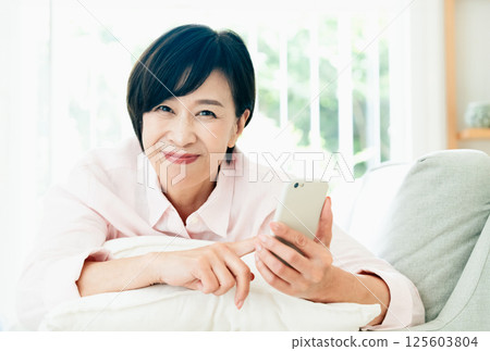 看在沙發的中部婦女一個智能手機 125603804