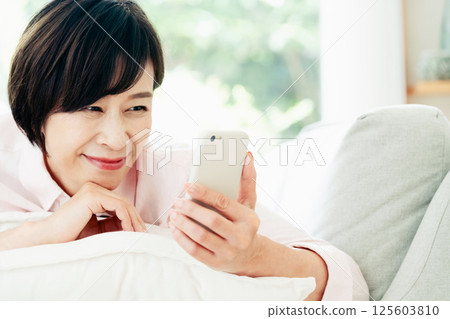 Middle woman looking at a smartphone on the sofa Middle woman looking at a smartphone on the sofa 125603810