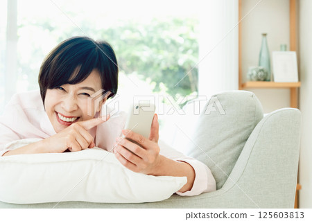 看在沙發的中部婦女一個智能手機 125603813
