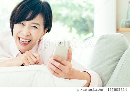 看在沙發的中部婦女一個智能手機 125603814