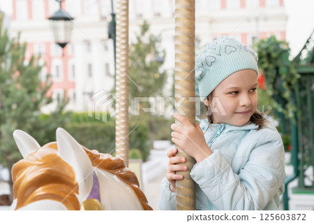 Little happy cute girl riding on carousel horse in park. Little girl have fun on carousel. 125603872