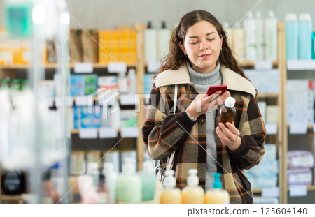 Girl in winter clothes scans code on cough syrup to check expiration date 125604140