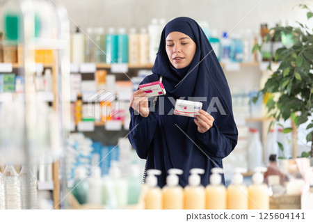 Young woman in Muslim attire comparing paracetamol packages at pharmacy 125604141