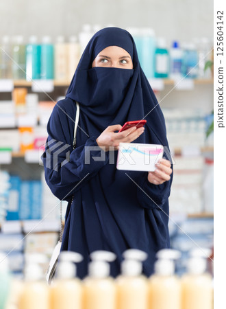 Young woman in hijab scans qr code of pills 125604142