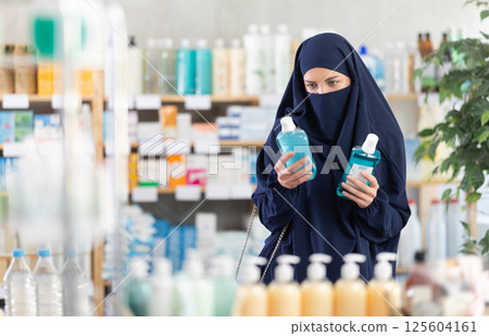 Female customer in Islamic clothing comparing two mouthwash products at drugstore Female customer in Islamic clothing comparing two mouthwash products at drugstore 125604161