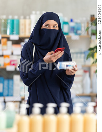 Young Muslim woman customer scanning QR-code on ointment box Young Muslim woman customer scanning QR-code on ointment box 125604162