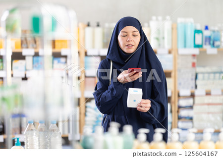 Young Muslim woman customer scanning QR-code on pills box 125604167