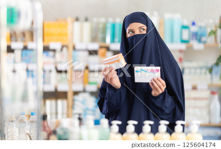 Young Muslim woman customer choosing pills in box in drugstore 125604174