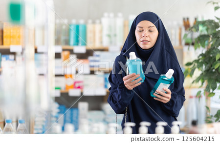 Female customer in Islamic clothing comparing two mouthwash products at drugstore Female customer in Islamic clothing comparing two mouthwash products at drugstore 125604215