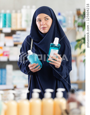Muslim woman in abaya and hijab choosing mouthwash in pharmacy 125604218