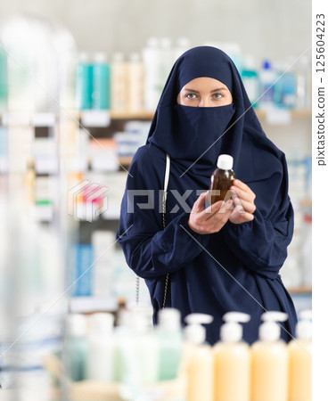 Young woman in hijab chooses syrup at pharmacy 125604223