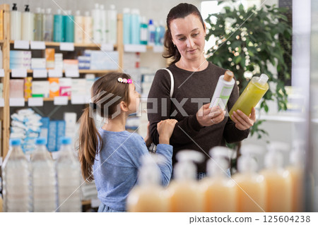 Woman with daughter choosing shampoo or shower gel Woman with daughter choosing shampoo or shower gel 125604238