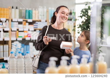 Woman with daughter choosing pills in pharmacy Woman with daughter choosing pills in pharmacy 125604240