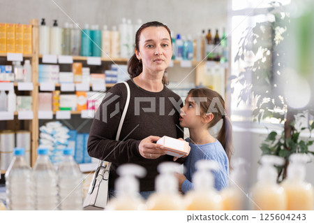 Woman with schoolgirl daughter are busy choosing tablet box at pharmacy Woman with schoolgirl daughter are busy choosing tablet box at pharmacy 125604243