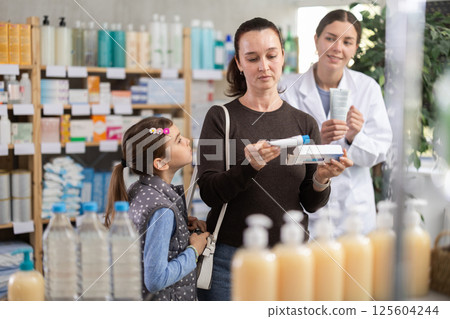 Middle-aged woman with daughter choosing ointment in drugstore Middle-aged woman with daughter choosing ointment in drugstore 125604244